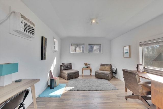 living area featuring lofted ceiling, plenty of natural light, wood finished floors, and a wall mounted air conditioner