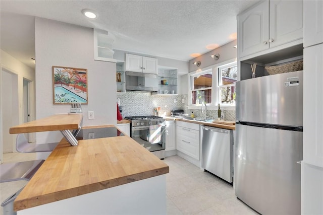 kitchen featuring open shelves, stainless steel appliances, butcher block counters, backsplash, and a sink