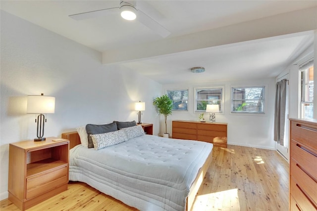 bedroom featuring light wood-type flooring, a ceiling fan, baseboards, and beamed ceiling