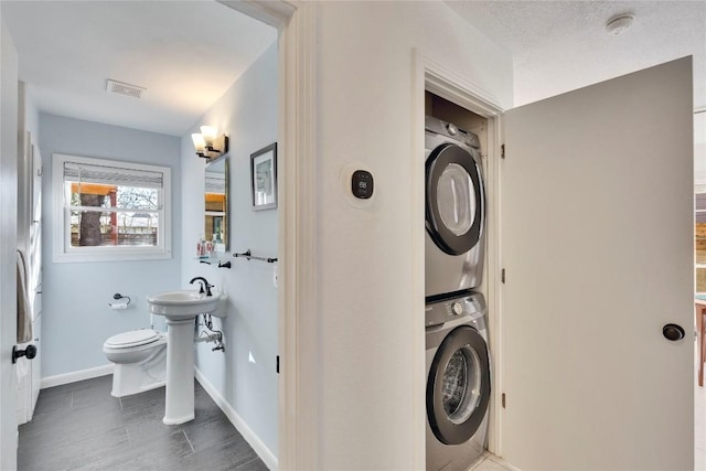 clothes washing area featuring stacked washer and dryer, baseboards, and visible vents