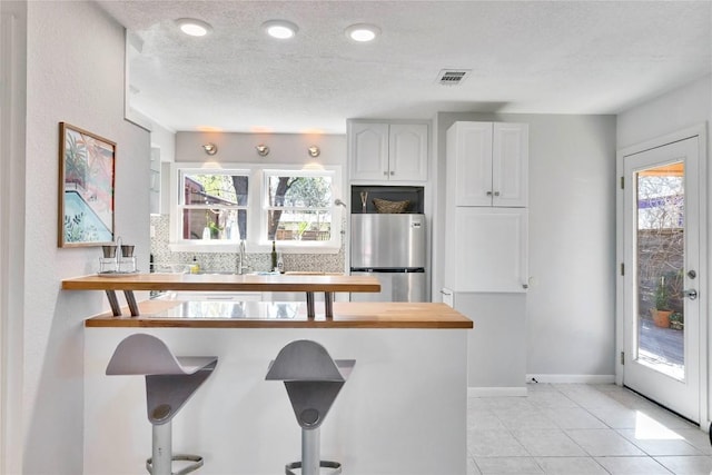 kitchen featuring freestanding refrigerator, white cabinets, a healthy amount of sunlight, and a kitchen breakfast bar