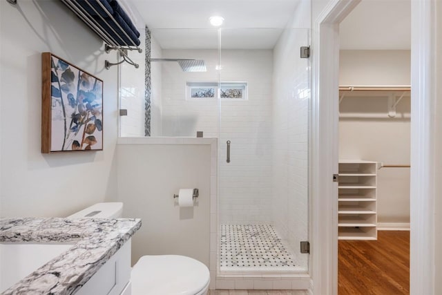 bathroom featuring wood finished floors, a shower stall, toilet, and a walk in closet