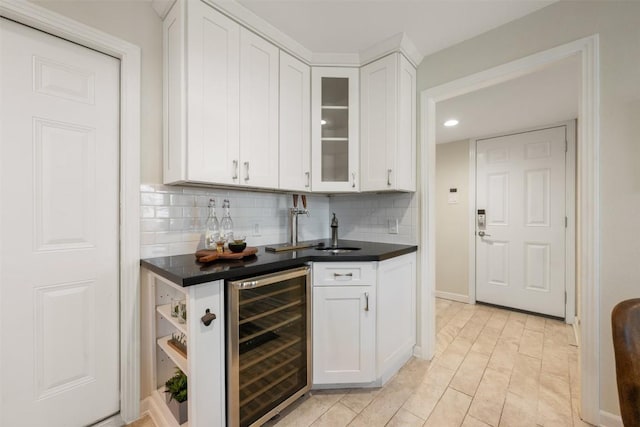 kitchen with beverage cooler, white cabinetry, backsplash, dark countertops, and glass insert cabinets