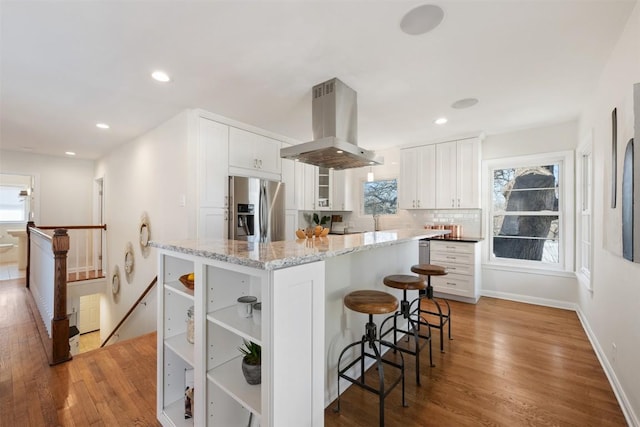 kitchen featuring backsplash, white cabinetry, stainless steel refrigerator with ice dispenser, and island range hood