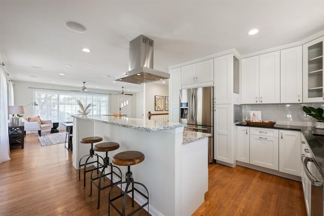 kitchen with island exhaust hood, wood finished floors, white cabinets, a kitchen bar, and glass insert cabinets