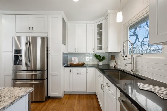 kitchen with light wood finished floors, tasteful backsplash, white cabinetry, a sink, and stainless steel fridge