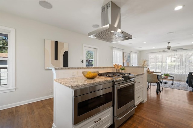 kitchen featuring island range hood, dark wood-type flooring, white cabinetry, appliances with stainless steel finishes, and light stone countertops