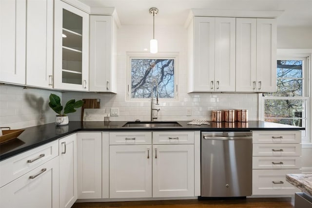 kitchen featuring stainless steel dishwasher, dark countertops, a sink, and white cabinets