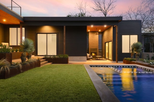 back of property at dusk with an outdoor pool, a yard, and a patio