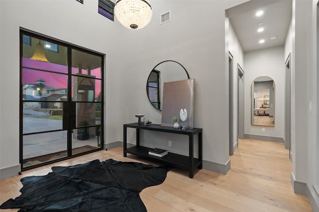 hallway with visible vents, arched walkways, light wood-style floors, and baseboards