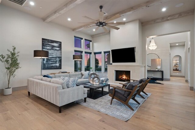 living area featuring arched walkways, a warm lit fireplace, and light wood-style flooring