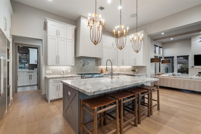 kitchen with light wood-type flooring, visible vents, tasteful backsplash, open floor plan, and light stone countertops