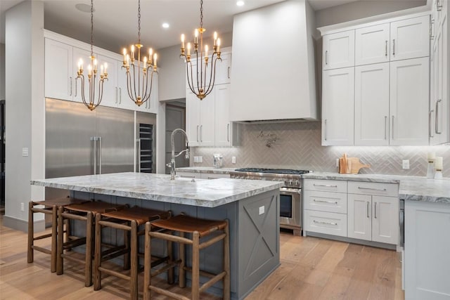 kitchen with high end range, white cabinetry, light wood-style floors, and a sink