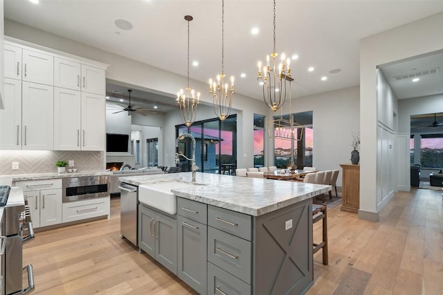 kitchen featuring gray cabinetry, light wood-style flooring, a sink, open floor plan, and white cabinets