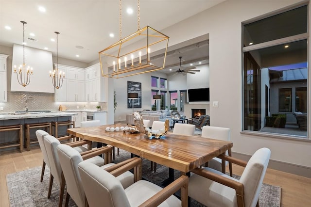 dining area with recessed lighting, ceiling fan with notable chandelier, light wood finished floors, and a lit fireplace