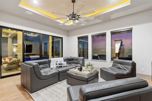 living room with light wood-type flooring, a raised ceiling, and a ceiling fan