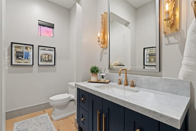 half bath with toilet, vanity, and wood finished floors