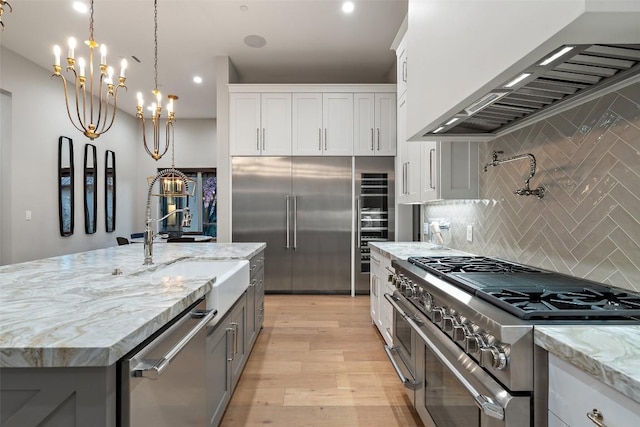 kitchen with light wood-style flooring, light stone counters, premium appliances, tasteful backsplash, and custom exhaust hood