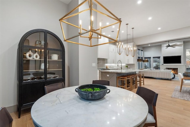 dining area with recessed lighting, ceiling fan with notable chandelier, a lit fireplace, and light wood finished floors