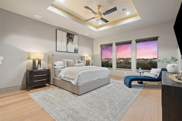 bedroom featuring visible vents, baseboards, a tray ceiling, ceiling fan, and light wood-type flooring