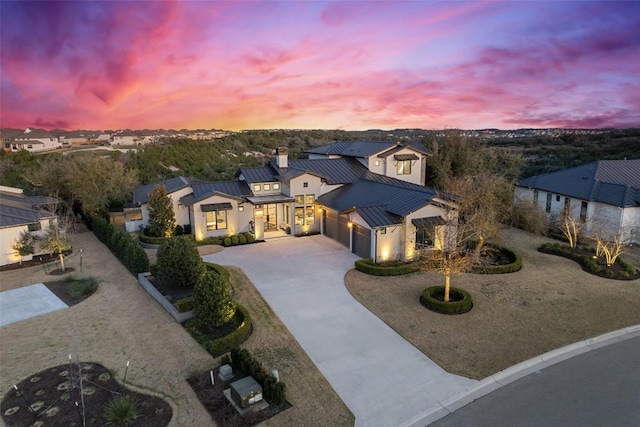 modern farmhouse featuring driveway, a standing seam roof, an attached garage, metal roof, and a chimney