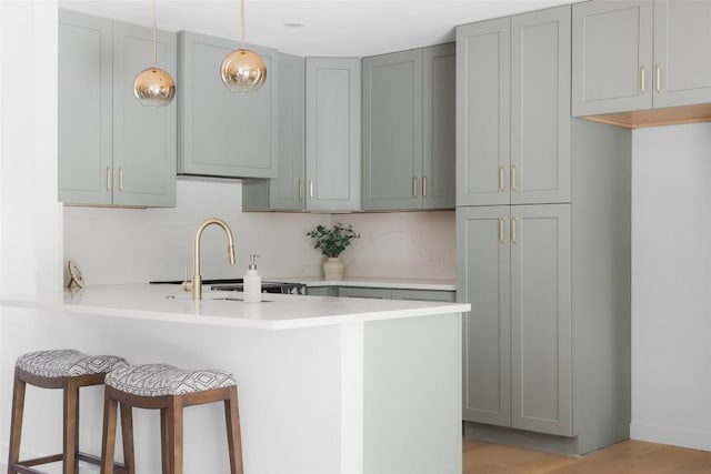 kitchen featuring a peninsula, a sink, a kitchen breakfast bar, light countertops, and pendant lighting