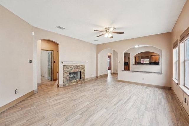 unfurnished living room featuring light wood finished floors, a stone fireplace, visible vents, and baseboards