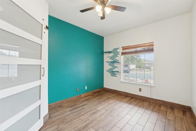 spare room with baseboards, a barn door, a ceiling fan, and wood finished floors