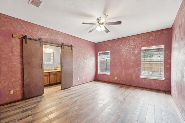 empty room featuring a barn door, light wood-type flooring, visible vents, and a ceiling fan