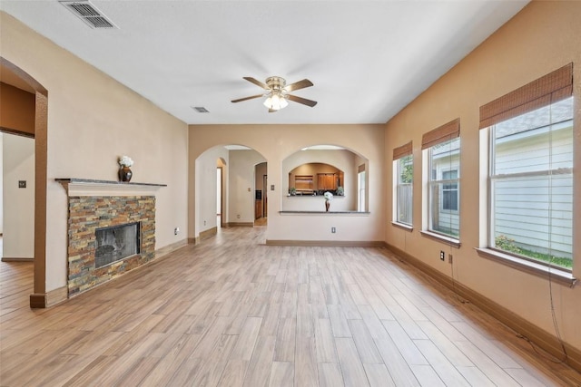 9316 Brents Elm Dr, Austin, TX 78744 - unfurnished living room featuring a ceiling fan, light wood-style floors, a stone fireplace, and arched walkways