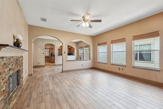 9316 Brents Elm Dr, Austin, TX 78744 - unfurnished living room featuring a ceiling fan, light wood-style flooring, arched walkways, and a fireplace