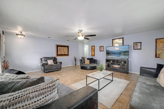 living room featuring a glass covered fireplace, tile patterned flooring, ceiling fan, and baseboards