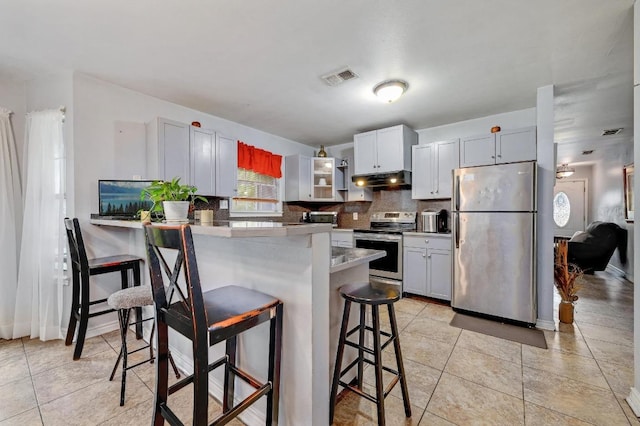 kitchen featuring visible vents, backsplash, appliances with stainless steel finishes, a peninsula, and a kitchen bar