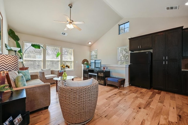 living area featuring light wood-style floors, a ceiling fan, visible vents, and high vaulted ceiling