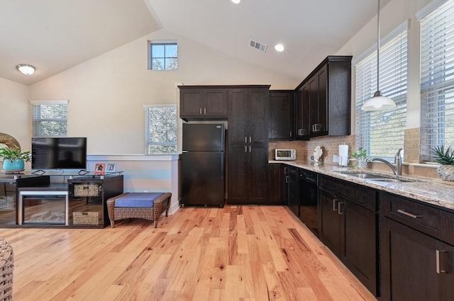 kitchen featuring visible vents, light stone counters, vaulted ceiling, black appliances, and a sink