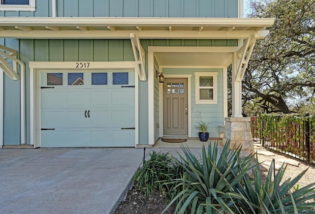 view of exterior entry with a garage, driveway, board and batten siding, and fence