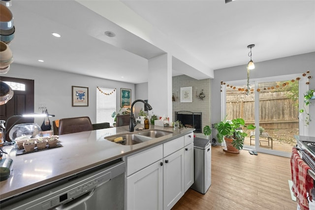 kitchen featuring a sink, white cabinetry, hanging light fixtures, appliances with stainless steel finishes, and light wood finished floors