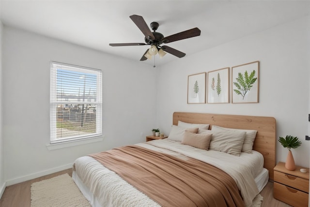 bedroom with light wood-type flooring, a ceiling fan, and baseboards