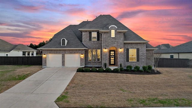 french country inspired facade with driveway, an attached garage, fence, and a lawn