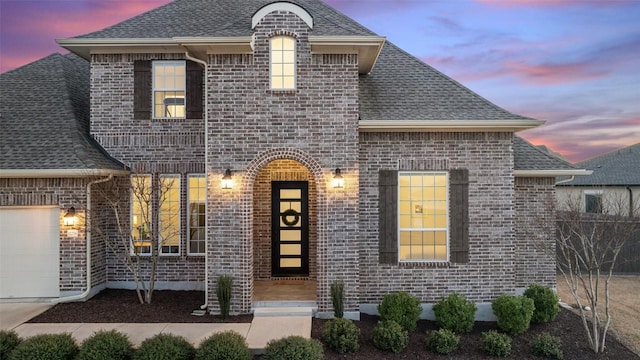 french provincial home featuring an attached garage, a shingled roof, fence, and brick siding