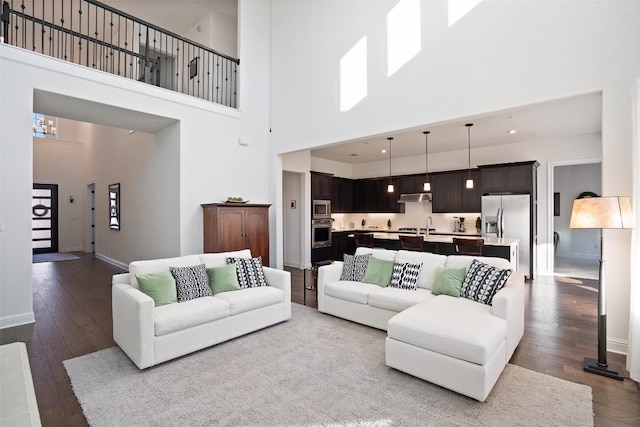 living area with dark wood-style floors, recessed lighting, a towering ceiling, and baseboards