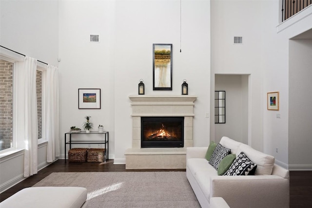 living room with a glass covered fireplace, visible vents, a towering ceiling, and baseboards