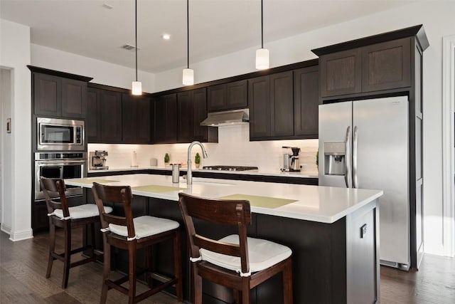 kitchen with light countertops, appliances with stainless steel finishes, backsplash, and under cabinet range hood