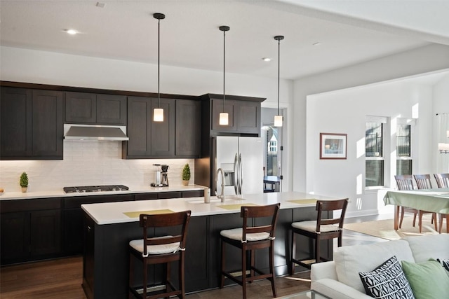 kitchen with under cabinet range hood, gas stovetop, light countertops, stainless steel refrigerator with ice dispenser, and decorative backsplash