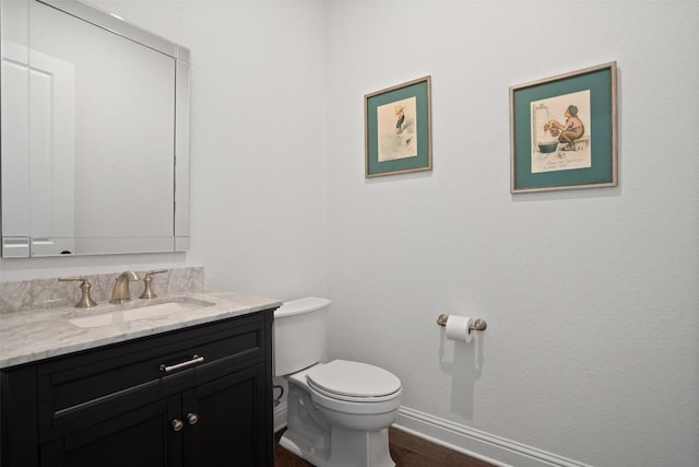 bathroom featuring toilet, baseboards, wood finished floors, and vanity