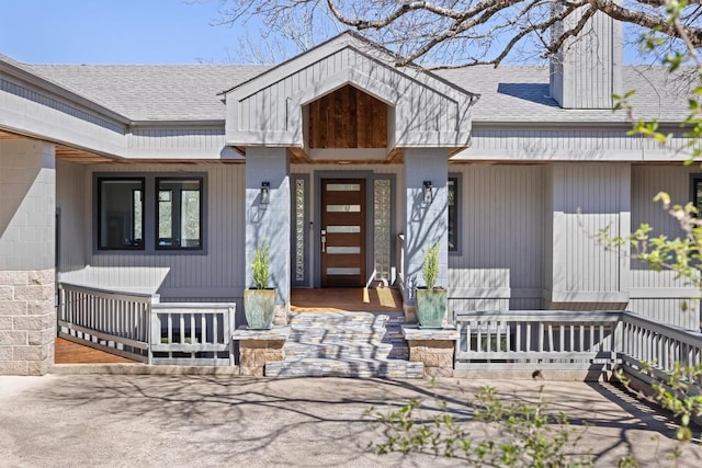 property entrance featuring concrete block siding, roof with shingles, and covered porch