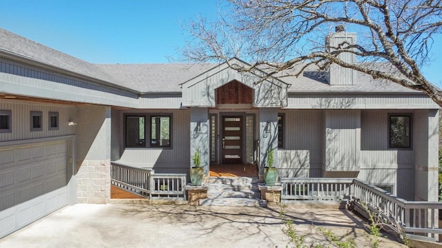 view of exterior entry with a porch, concrete driveway, and roof with shingles