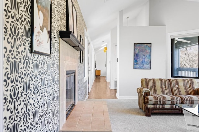 living area featuring light carpet, high vaulted ceiling, a tiled fireplace, and baseboards