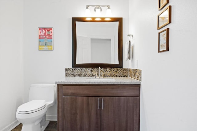 half bathroom with baseboards, toilet, vanity, and decorative backsplash