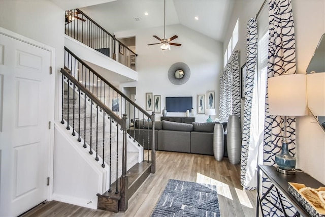 living room with ceiling fan, high vaulted ceiling, recessed lighting, wood finished floors, and stairway